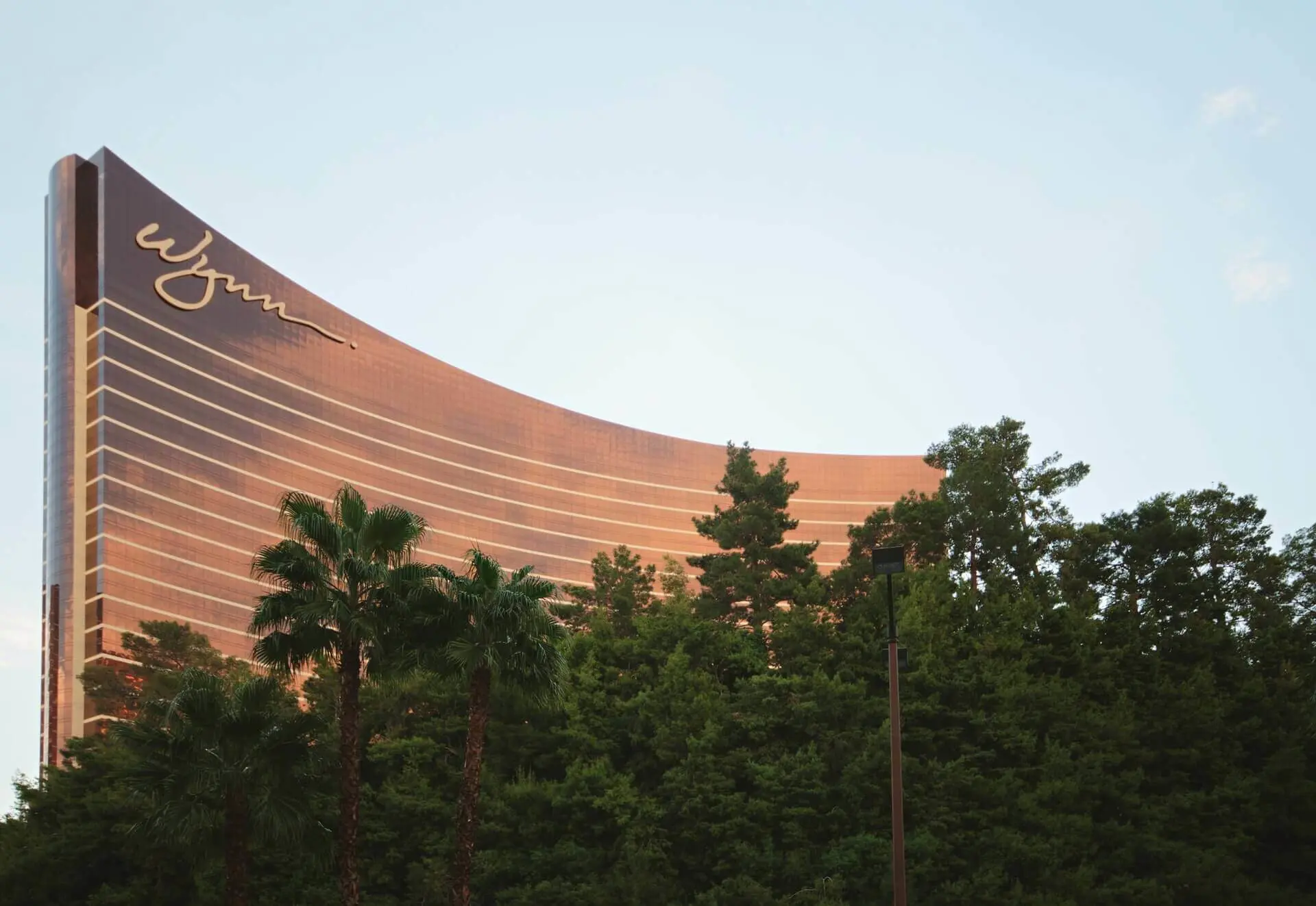 Image shows the golden looking Wynn casino and hotel in Las Vegas peeking out over some palm trees