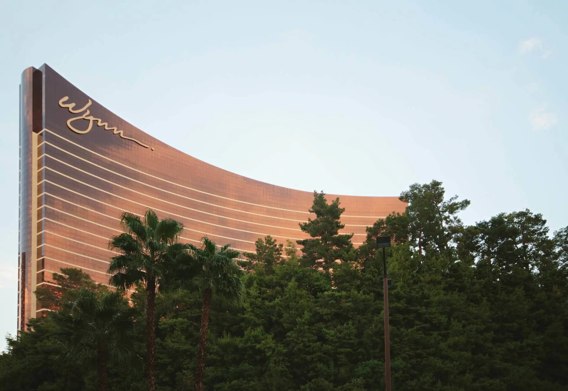 Image shows the golden looking Wynn casino and hotel in Las Vegas peeking out over some palm trees 